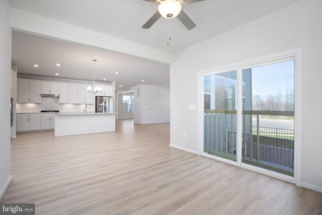 unfurnished living room with ceiling fan with notable chandelier and light wood-type flooring