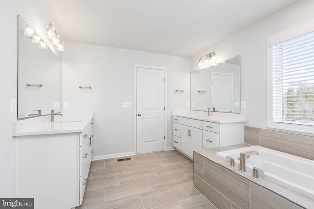 bathroom featuring a healthy amount of sunlight, vanity, and tiled tub