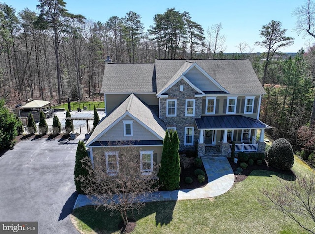 view of front facade with a chimney, stone siding, a porch, a front yard, and a standing seam roof