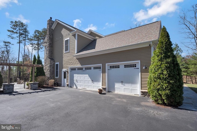view of side of home featuring a chimney, an attached garage, aphalt driveway, and a shingled roof