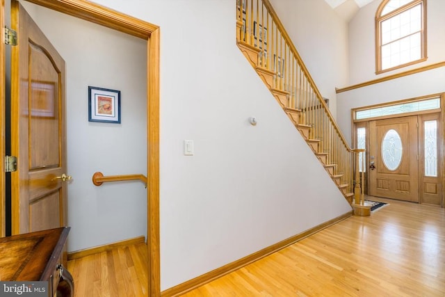 foyer entrance with a towering ceiling, stairway, baseboards, and wood finished floors