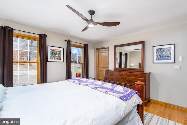 bedroom featuring a ceiling fan, multiple windows, baseboards, and wood finished floors