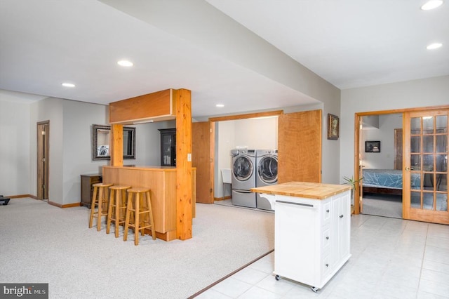 kitchen with a breakfast bar, washing machine and clothes dryer, wood counters, and recessed lighting