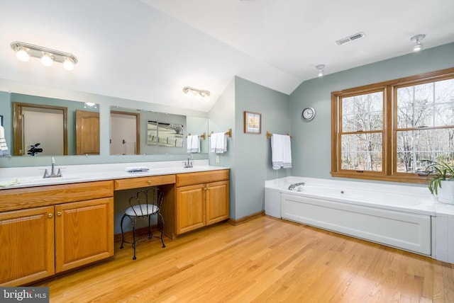 full bathroom with lofted ceiling, wood finished floors, visible vents, a bath, and double vanity