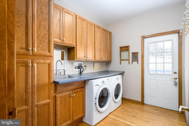 laundry room with cabinet space, light wood finished floors, baseboards, washing machine and dryer, and a sink