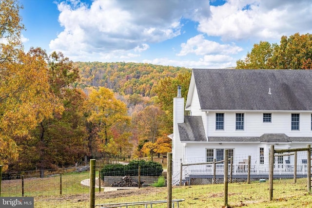 exterior space with fence, a yard, roof with shingles, a wooden deck, and a chimney