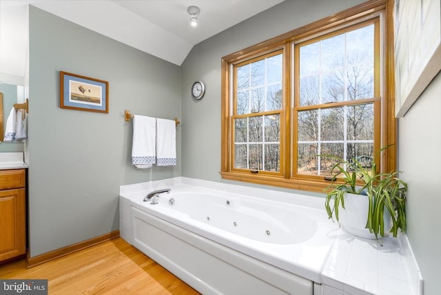 bathroom featuring baseboards, lofted ceiling, a tub with jets, wood finished floors, and vanity