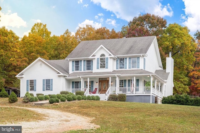 colonial home with a chimney, a front lawn, a porch, and roof with shingles