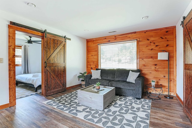 living room featuring dark wood-type flooring, plenty of natural light, a barn door, and wood walls