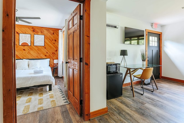 bedroom featuring dark hardwood / wood-style flooring, black refrigerator, a wall mounted AC, and wooden walls