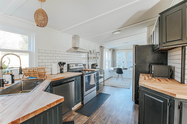 kitchen with butcher block countertops, sink, hanging light fixtures, stainless steel appliances, and ventilation hood