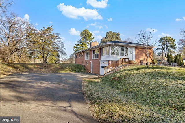 view of front of home with a front yard, an attached garage, a chimney, aphalt driveway, and brick siding