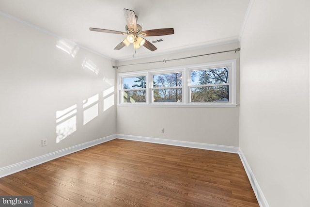 spare room with a ceiling fan, wood finished floors, visible vents, baseboards, and crown molding