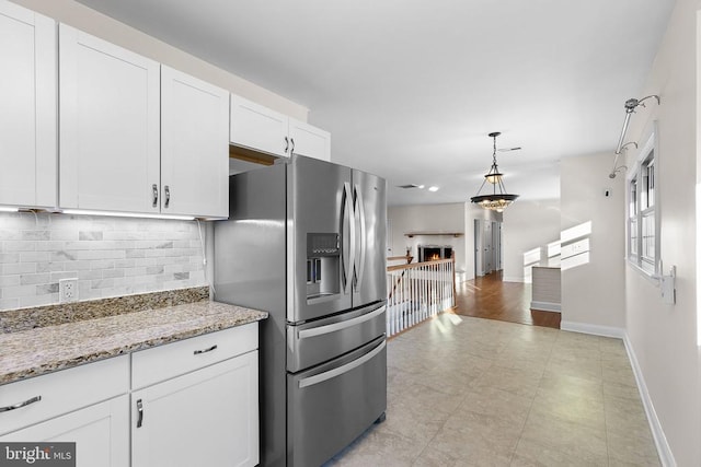 kitchen featuring tasteful backsplash, a lit fireplace, hanging light fixtures, stainless steel fridge, and white cabinetry