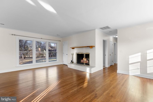 unfurnished living room with wood finished floors, a fireplace, visible vents, and baseboards