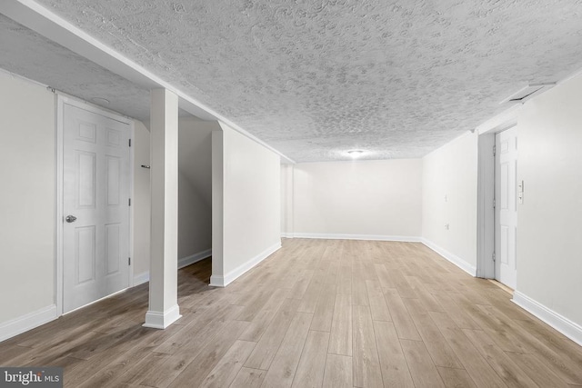 finished below grade area with a textured ceiling, baseboards, and wood finished floors