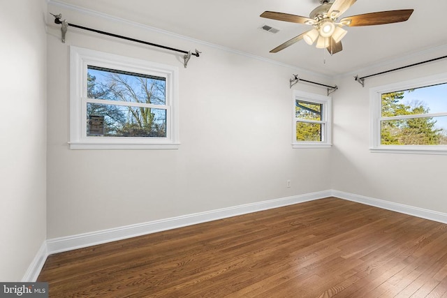 empty room featuring visible vents, ornamental molding, dark wood-style floors, baseboards, and ceiling fan