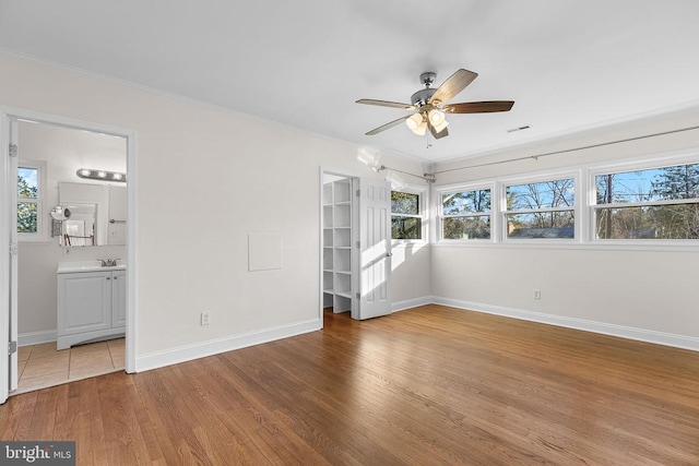 unfurnished bedroom featuring visible vents, ornamental molding, a sink, wood finished floors, and baseboards