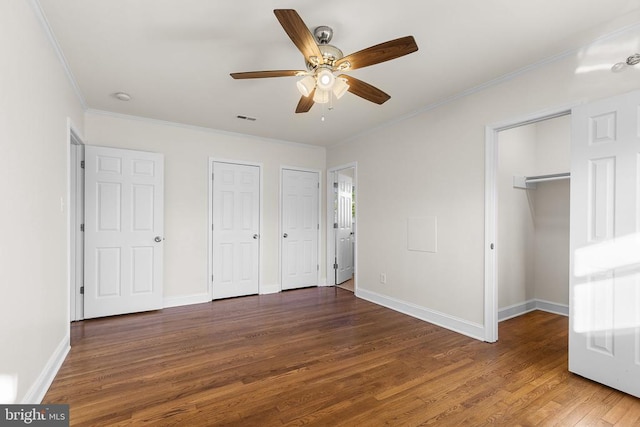 unfurnished bedroom featuring visible vents, baseboards, multiple closets, ornamental molding, and wood finished floors