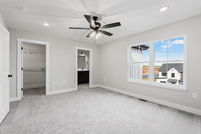 unfurnished bedroom featuring ensuite bath, a spacious closet, light colored carpet, a closet, and ceiling fan