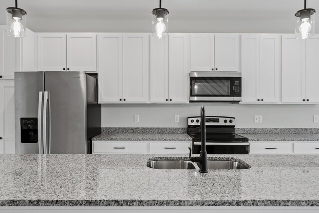 kitchen featuring hanging light fixtures, white cabinetry, appliances with stainless steel finishes, and light stone countertops