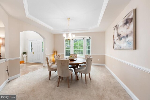 dining area featuring a raised ceiling, ornamental molding, light carpet, and a notable chandelier