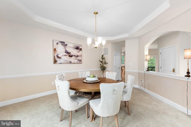 carpeted dining space with an inviting chandelier, a tray ceiling, and ornamental molding