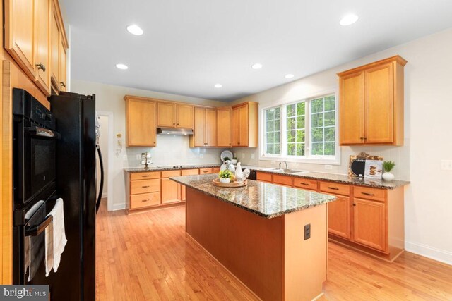 kitchen with light stone countertops, a center island, light wood-type flooring, and black appliances