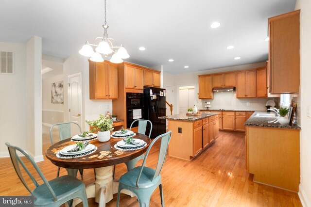 kitchen with pendant lighting, dark stone countertops, a center island, light hardwood / wood-style floors, and black refrigerator with ice dispenser