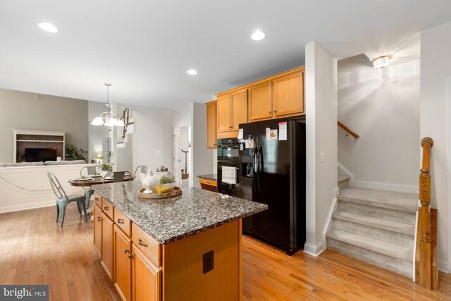 kitchen featuring dark stone countertops, a center island, black appliances, an inviting chandelier, and light hardwood / wood-style flooring