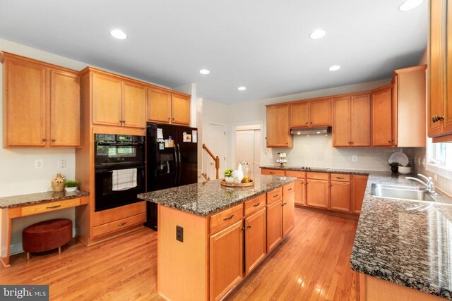 kitchen featuring sink, light hardwood / wood-style flooring, dark stone countertops, black appliances, and a kitchen island