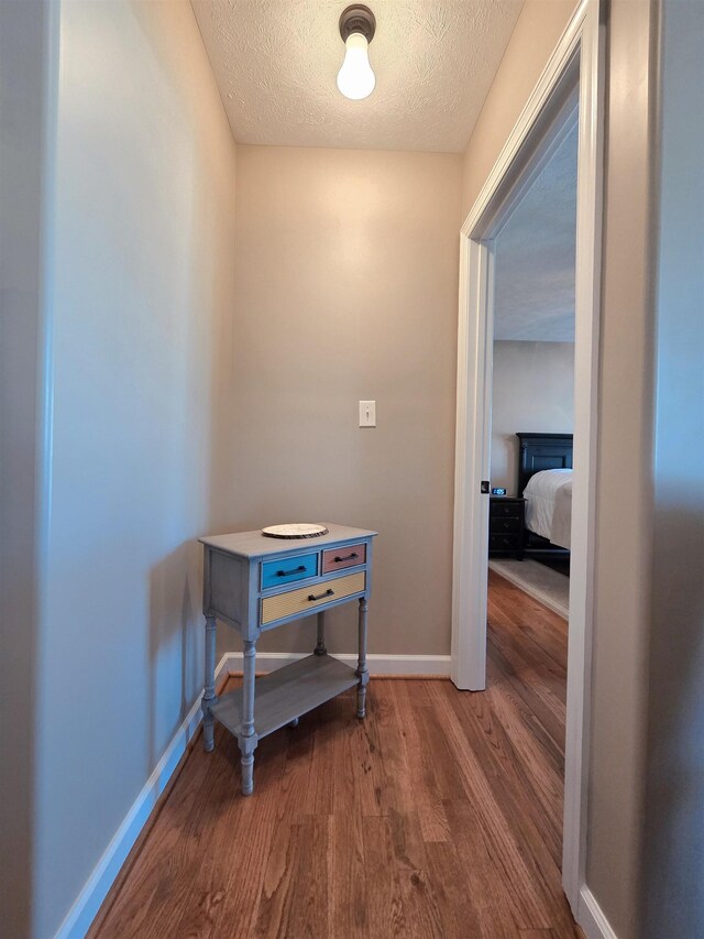 hallway featuring baseboards, wood finished floors, and a textured ceiling