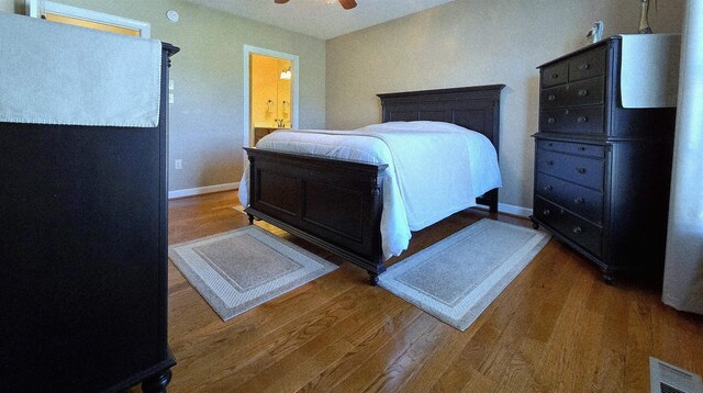 bedroom with wood finished floors, visible vents, baseboards, ceiling fan, and ensuite bathroom