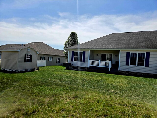 back of property featuring a lawn, a shingled roof, and covered porch