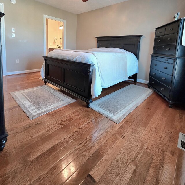 bedroom with baseboards, wood finished floors, and connected bathroom