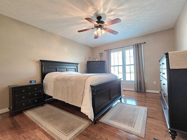 bedroom featuring wood finished floors, a textured ceiling, a ceiling fan, and baseboards