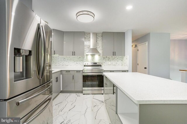 kitchen with wall chimney range hood, gray cabinets, appliances with stainless steel finishes, a center island, and decorative backsplash