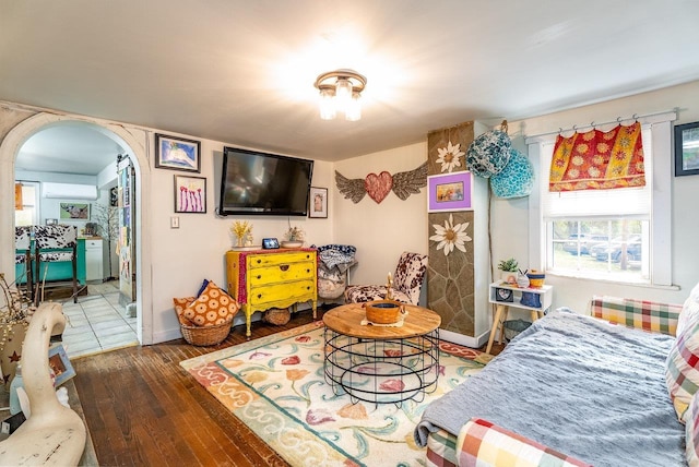 bedroom featuring wood-type flooring, arched walkways, a wall unit AC, and baseboards