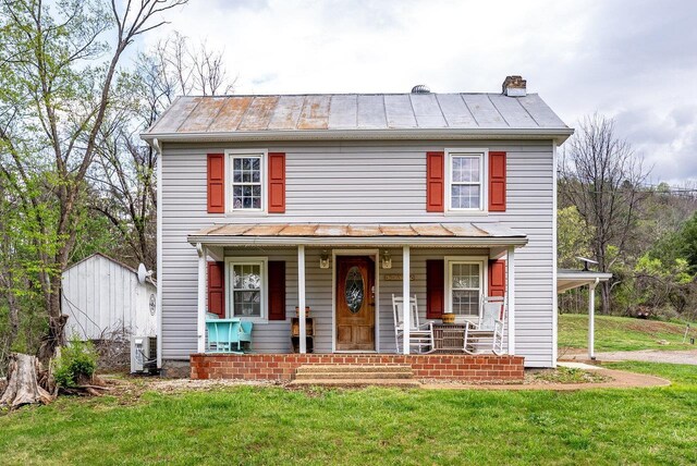 view of front of house with a standing seam roof, a chimney, covered porch, metal roof, and a front yard