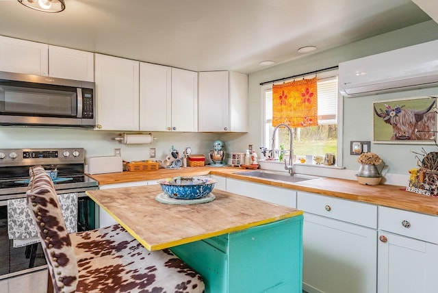 kitchen with butcher block countertops, a sink, a wall mounted AC, stainless steel appliances, and white cabinets