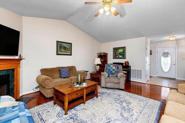 living room with vaulted ceiling, ceiling fan, a fireplace, and light hardwood / wood-style flooring