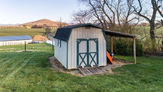 view of outbuilding featuring a rural view, a mountain view, and a yard