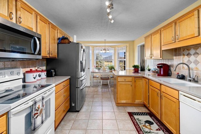 kitchen with sink, appliances with stainless steel finishes, light tile patterned flooring, decorative light fixtures, and kitchen peninsula