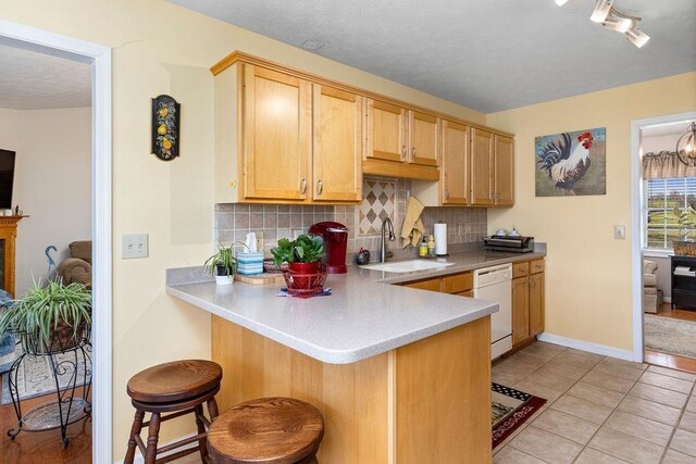 kitchen with a breakfast bar, sink, light brown cabinets, white dishwasher, and backsplash