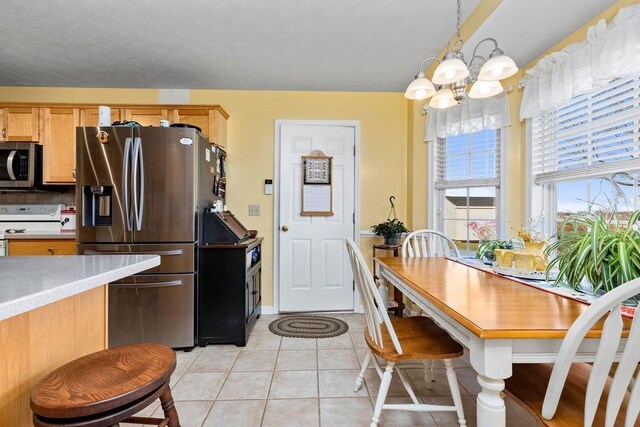 kitchen featuring light brown cabinetry, decorative light fixtures, light tile patterned floors, a notable chandelier, and stainless steel appliances