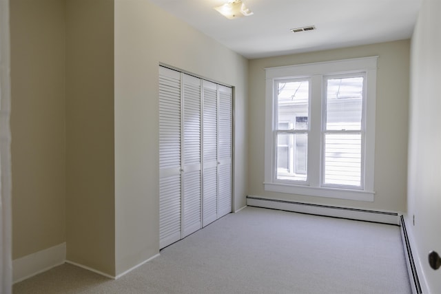 unfurnished bedroom featuring multiple windows, a baseboard radiator, light colored carpet, and a closet