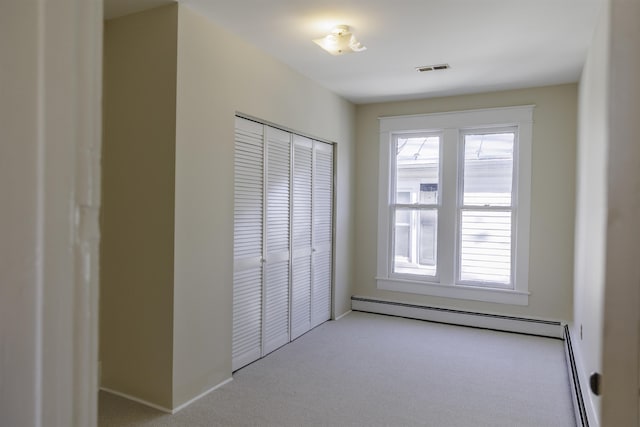 unfurnished bedroom featuring baseboard heating, light colored carpet, and a closet