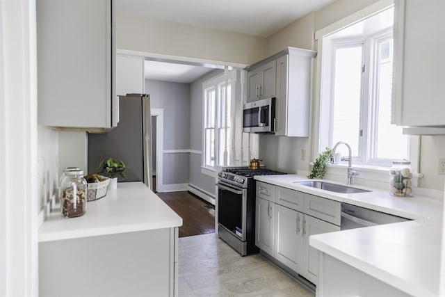 kitchen featuring baseboard heating, stainless steel appliances, sink, and gray cabinetry