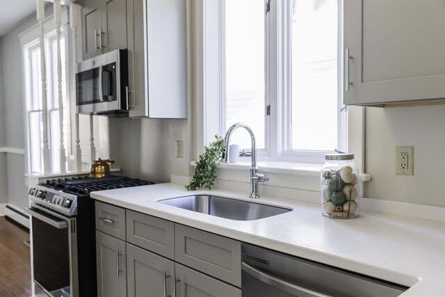 kitchen with dark wood-type flooring, sink, gray cabinetry, baseboard heating, and stainless steel appliances