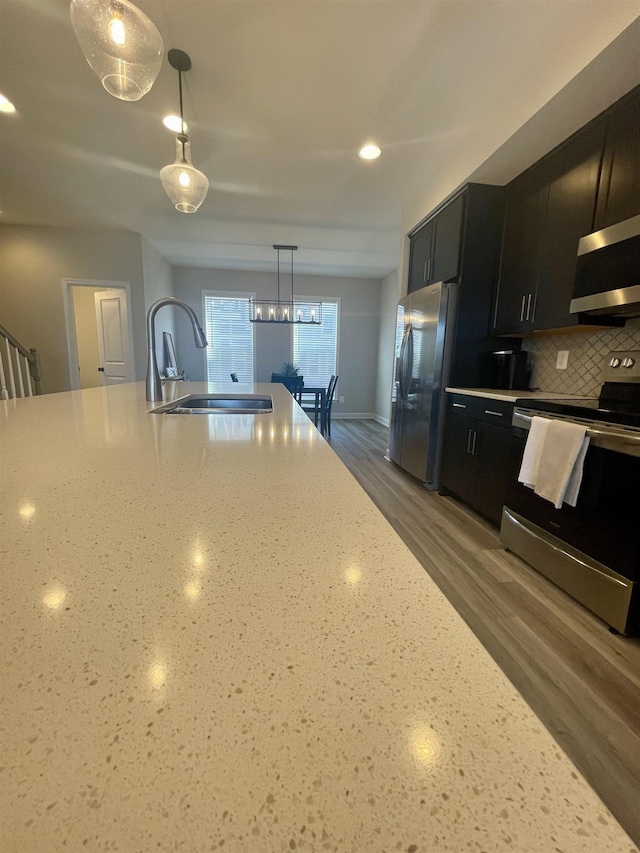 kitchen featuring sink, backsplash, decorative light fixtures, stainless steel appliances, and light stone countertops